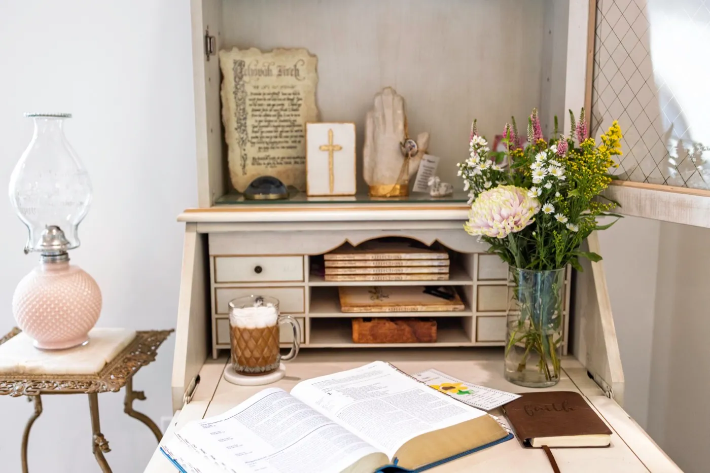 A secretary desk with an open book, coffee, and fresh flowers